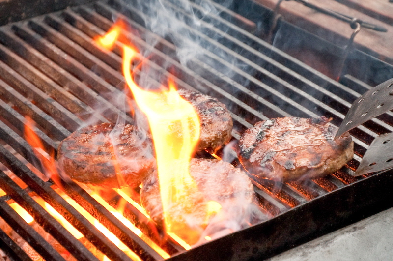 tasty burgers being cooked on a flaming barbecue